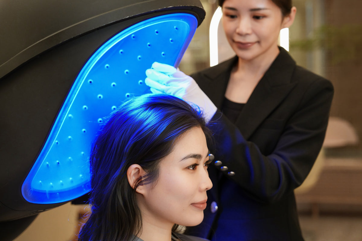 A client under an LED light therapy canopy with a TrichoLab specialist