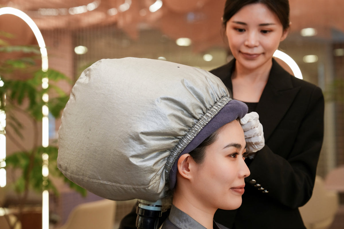 A client under a steam cap with a TrichoLab specialist beside her