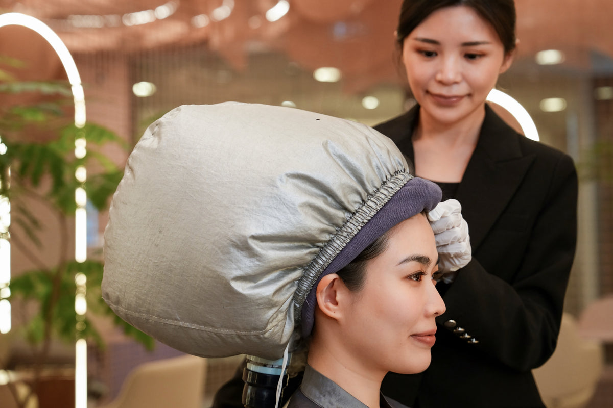 A client under a steam cap with a TrichoLab specialist beside her