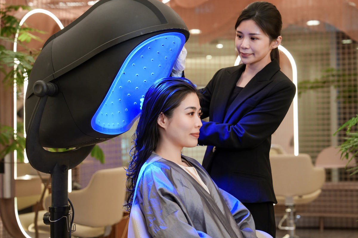 A client under an LED light therapy canopy with a TrichoLab specialist