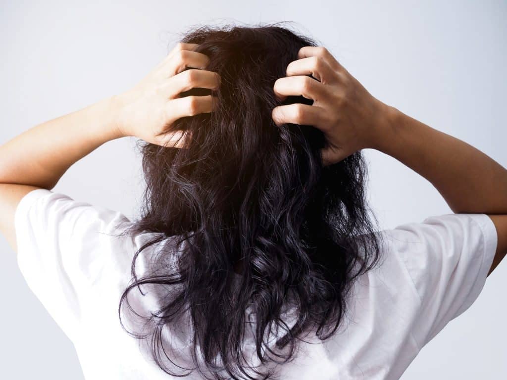 Woman with scalp acne scratching her head.