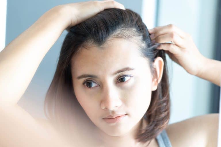 A woman looking at a bald patch on her scalp in the mirror