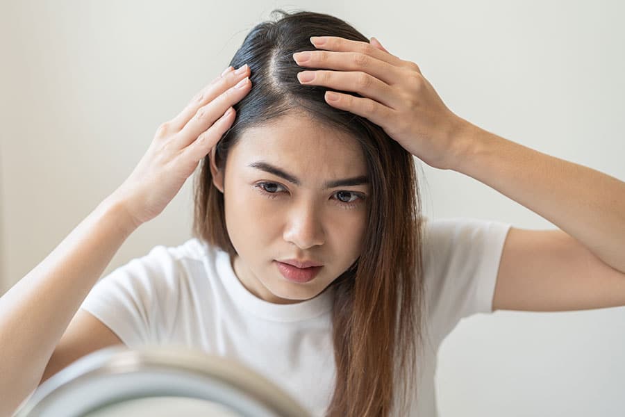 A woman with coloured hair looking at her scalp in the mirror.